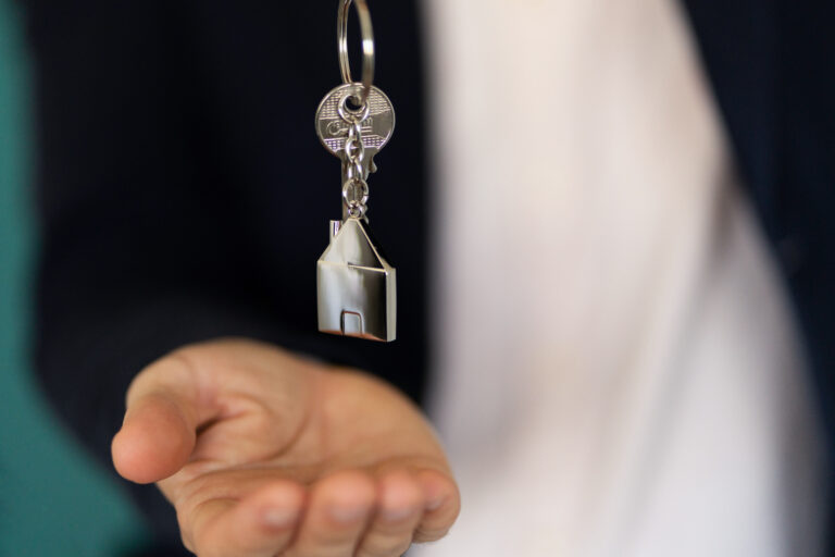 uitgestoken hand overhandigt sleutel met huisvormige sleutelhanger