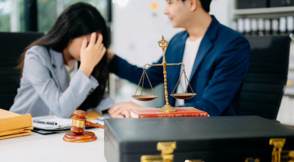 vrouw met handen voor haar gezicht naast een advocaat, weegschaal en hamer op tafel