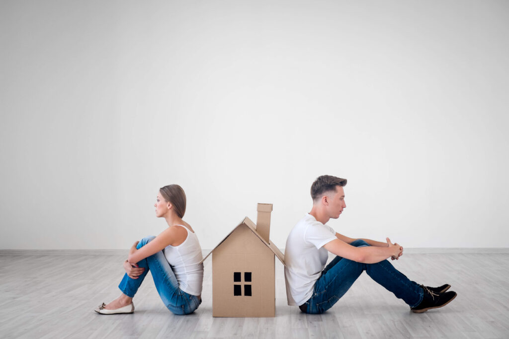 vrouw en man zitten met de rug naar elkaar bij een kartonnen huisje