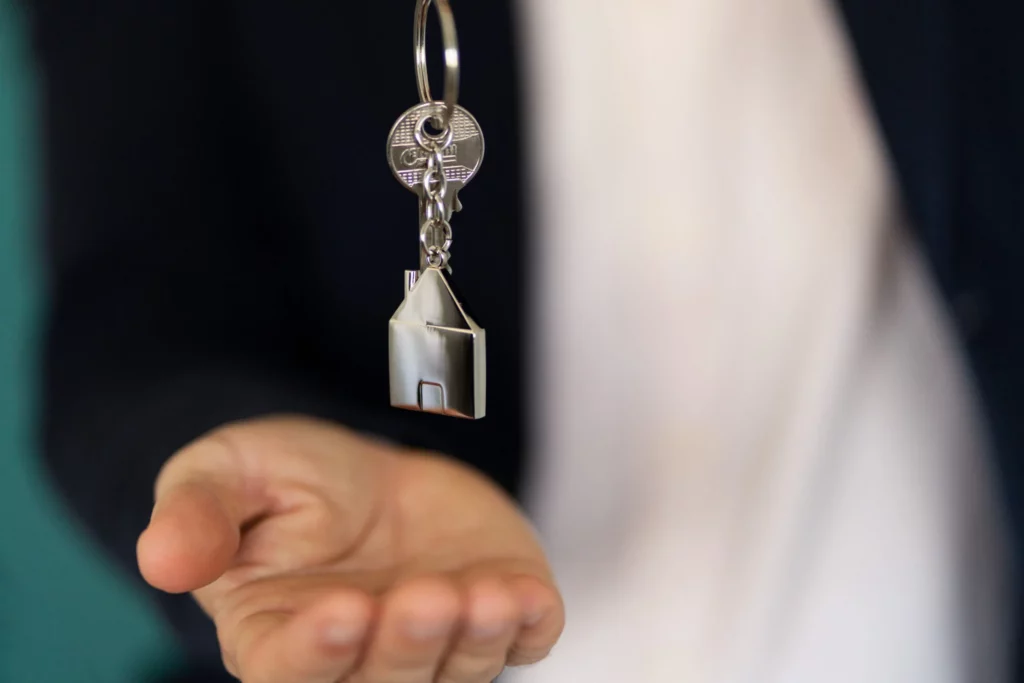 uitgestoken hand met een sleutel aan een huisvormige sleutelhanger