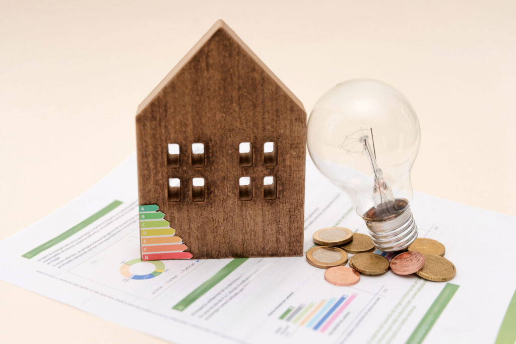 houten huisje met gloeilamp en munten op een energierapport met labelschaal A tot G