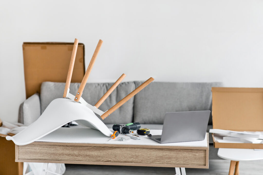 half gemonteerde stoel met boormachine, meetlint en laptop tussen verhuisdozen